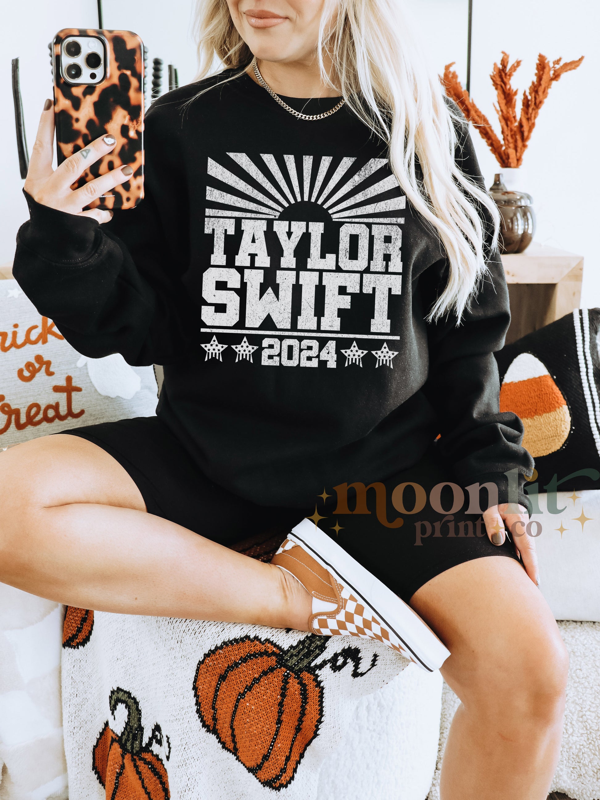 a woman sitting on a couch wearing a black taylor swift sweatshirt