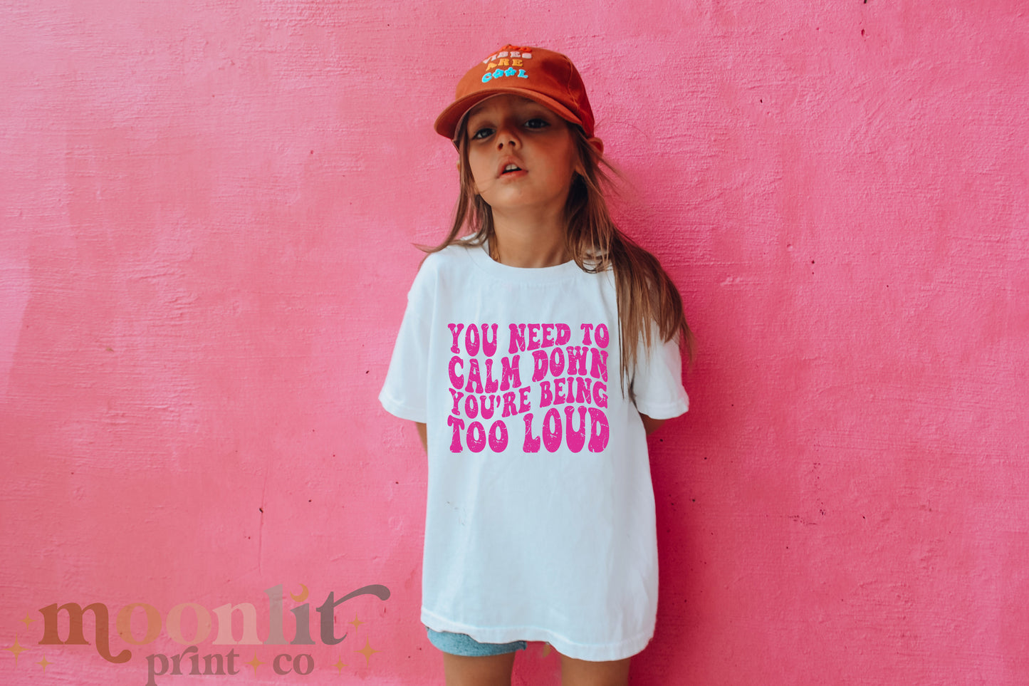 a little girl standing against a pink wall