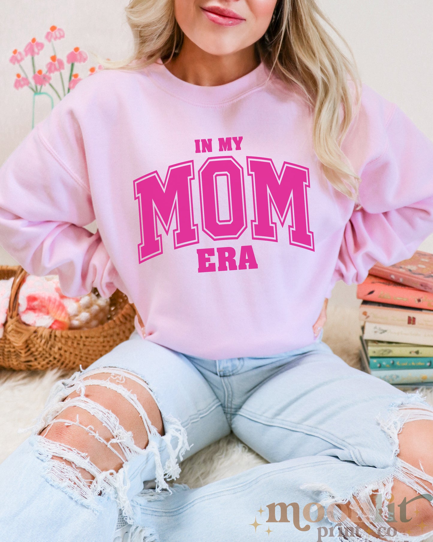 a woman wearing a pink sweatshirt that says in my mom era