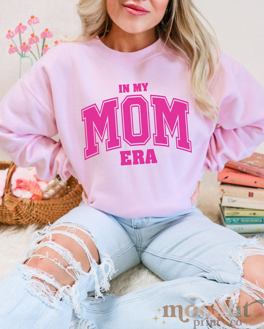 a woman wearing a pink sweatshirt that says in my mom era