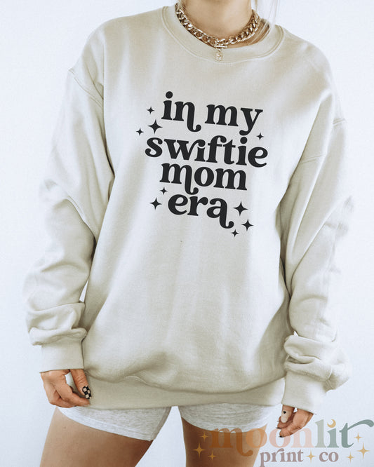 a woman wearing a sweatshirt that says in my swiffie mom era