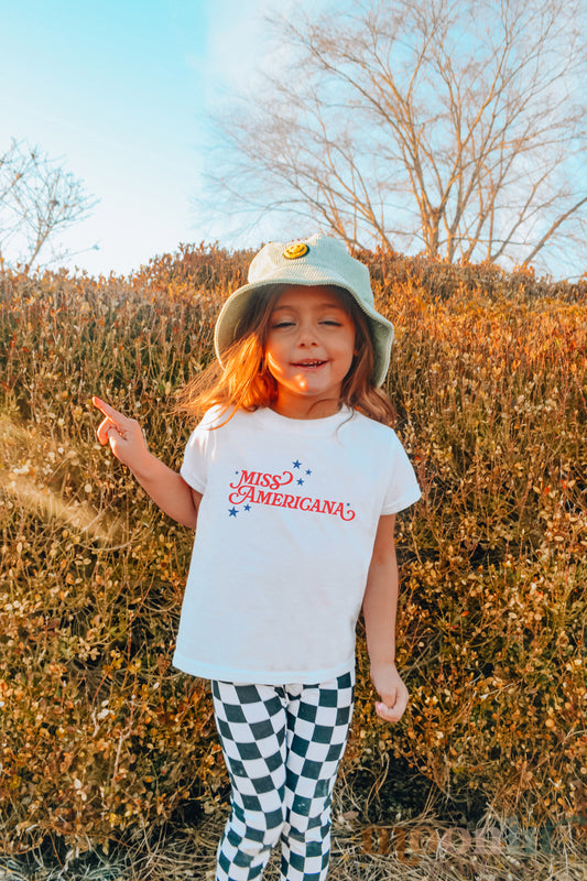 a little girl standing in front of a bush