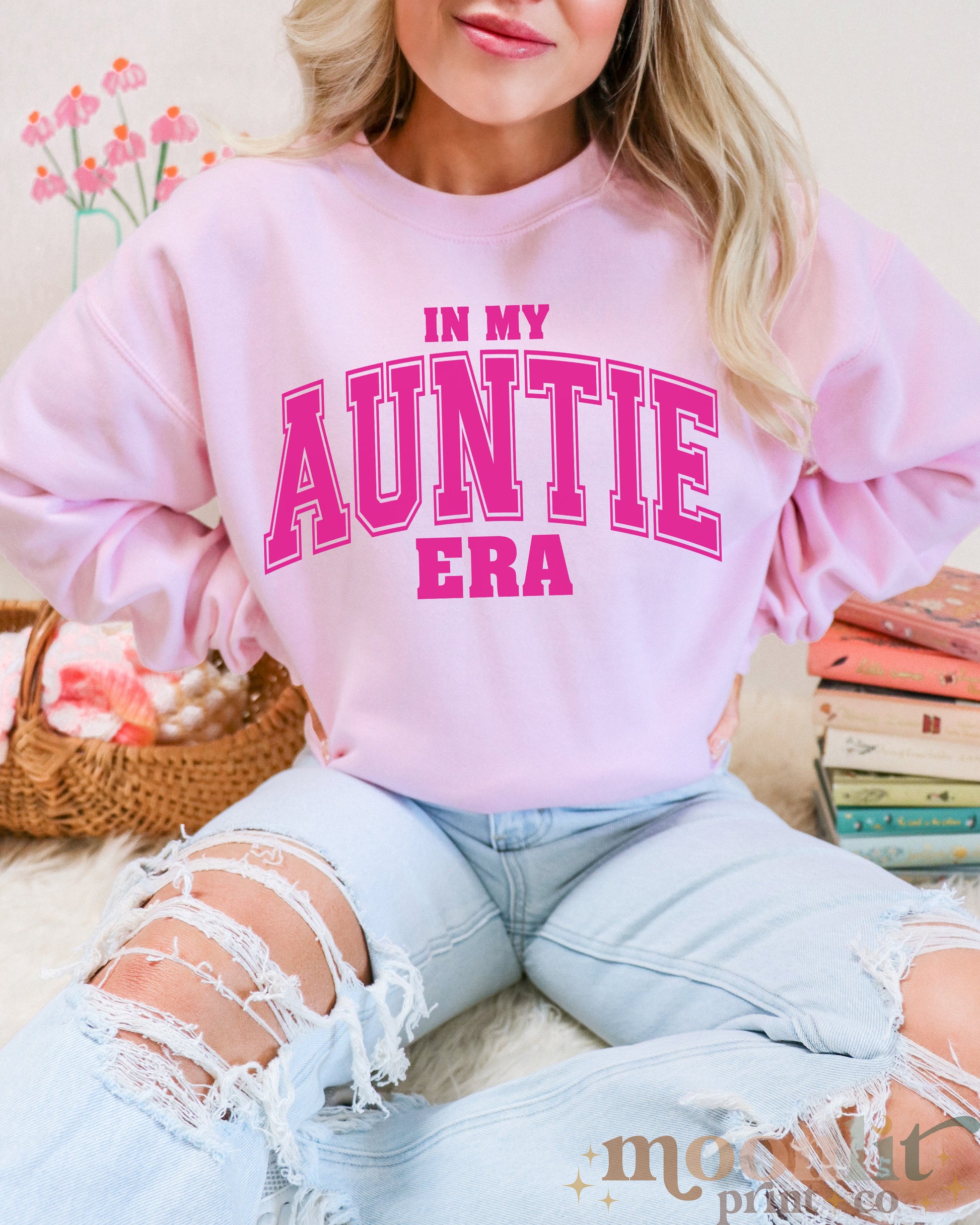 a woman sitting on a bed wearing a pink sweatshirt