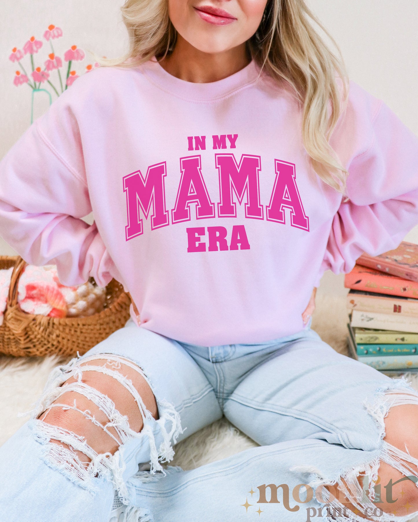 a woman wearing a pink sweatshirt that says in my mama era