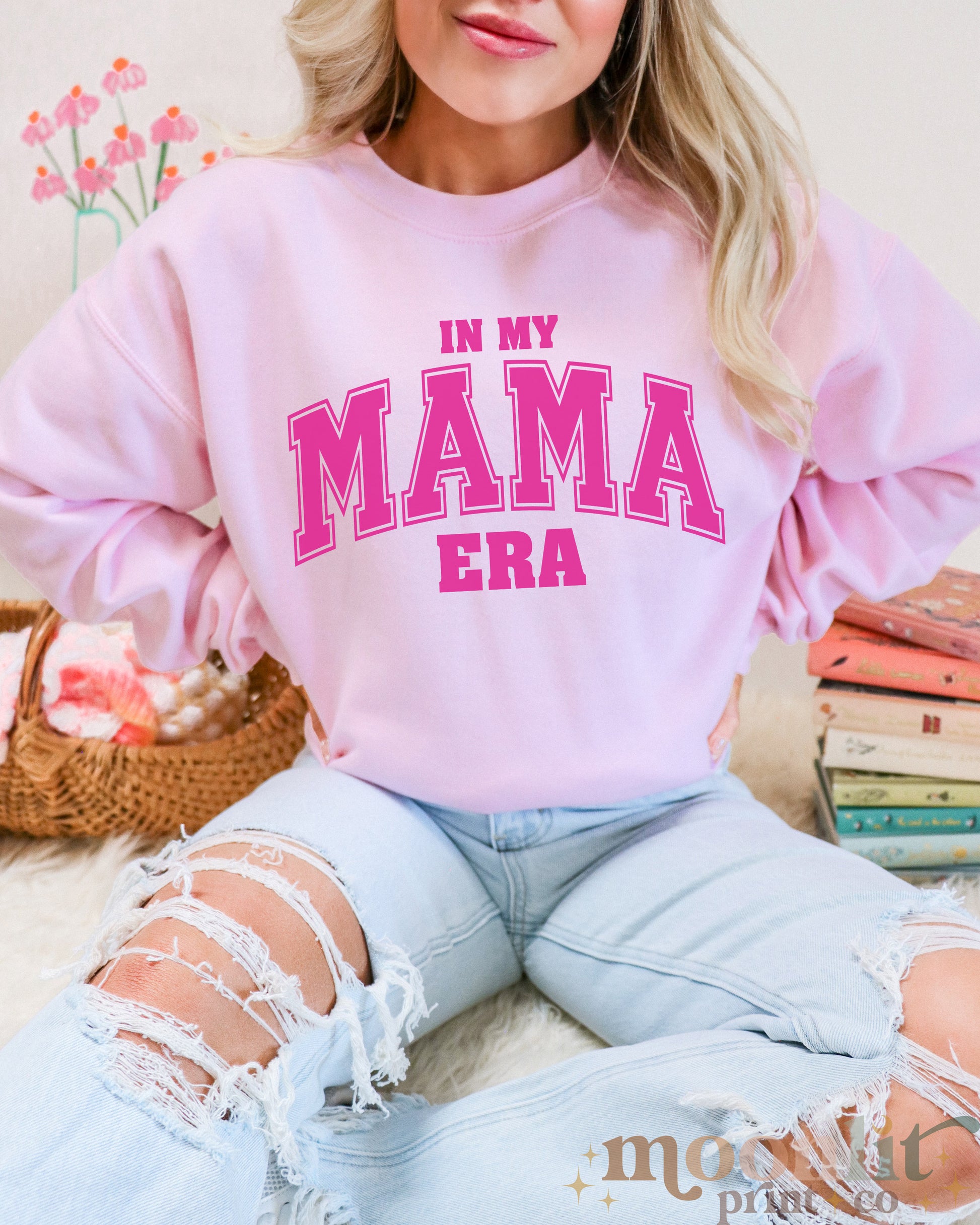 a woman wearing a pink sweatshirt that says in my mama era