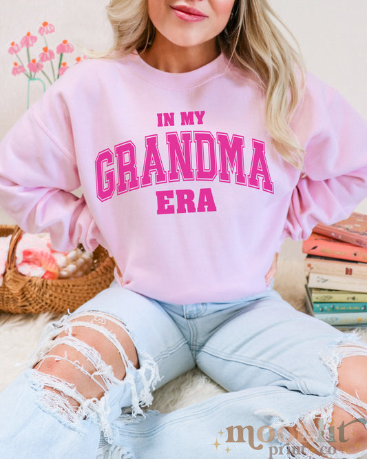 a woman sitting on a bed wearing a pink sweatshirt